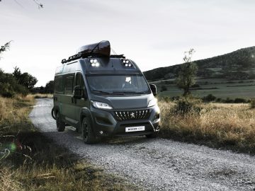 Een zwarte Peugeot Boxer rijdt over een onverharde weg.