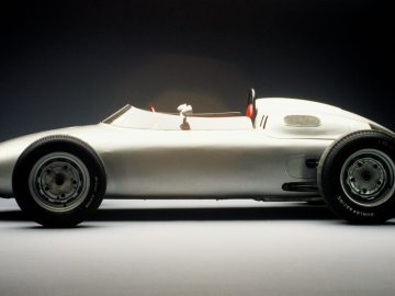 Op een donkere achtergrond is een zilveren Porsche-raceauto afgebeeld.