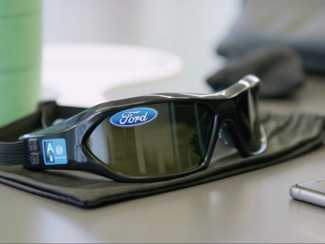 Een Ford-slaappak-bril op een bureau naast een mobiele telefoon.