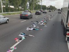 Een stapel kleding aan de kant van een snelweg, gemarkeerd met een bordje slipgevaar.