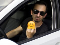 Een automobilist zit in een auto met een smiley op zijn gezicht.