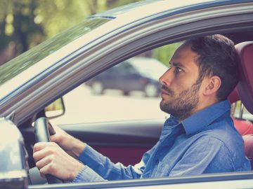 Een man bestuurt een auto met zijn handen aan het stuur en bereidt zich voor op het Theorie-examen auto.