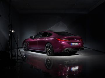 Een paarse BMW M8 Gran Coupé in een donkere kamer.