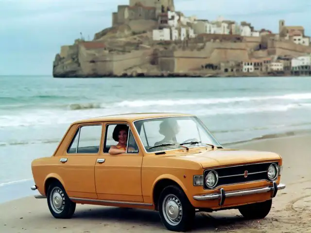 Op het strand staat een gele Fiat 128 geparkeerd.