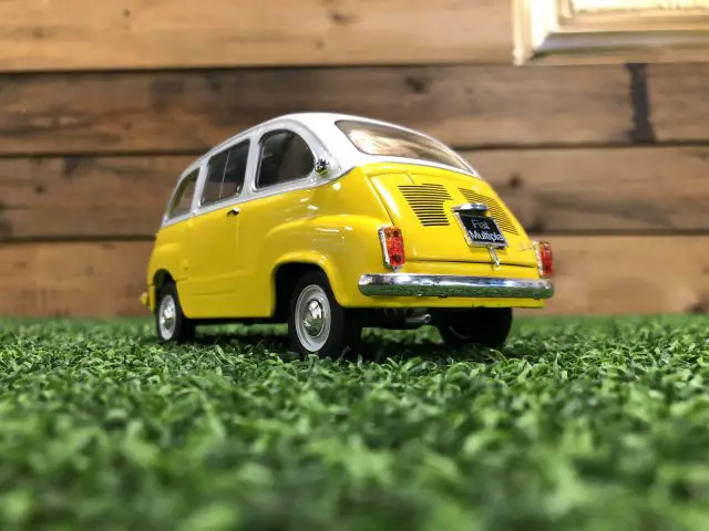 Op het gras staat een gele Fiat 600 Multipla speelgoedauto geparkeerd.