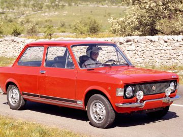 Er rijdt een rode Fiat 128 over de weg.