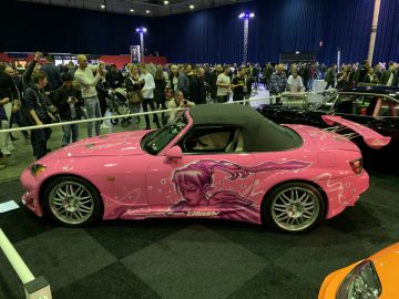 Een roze sportwagen is te zien op de 100% Auto Live 2019 in een menigte mensen.