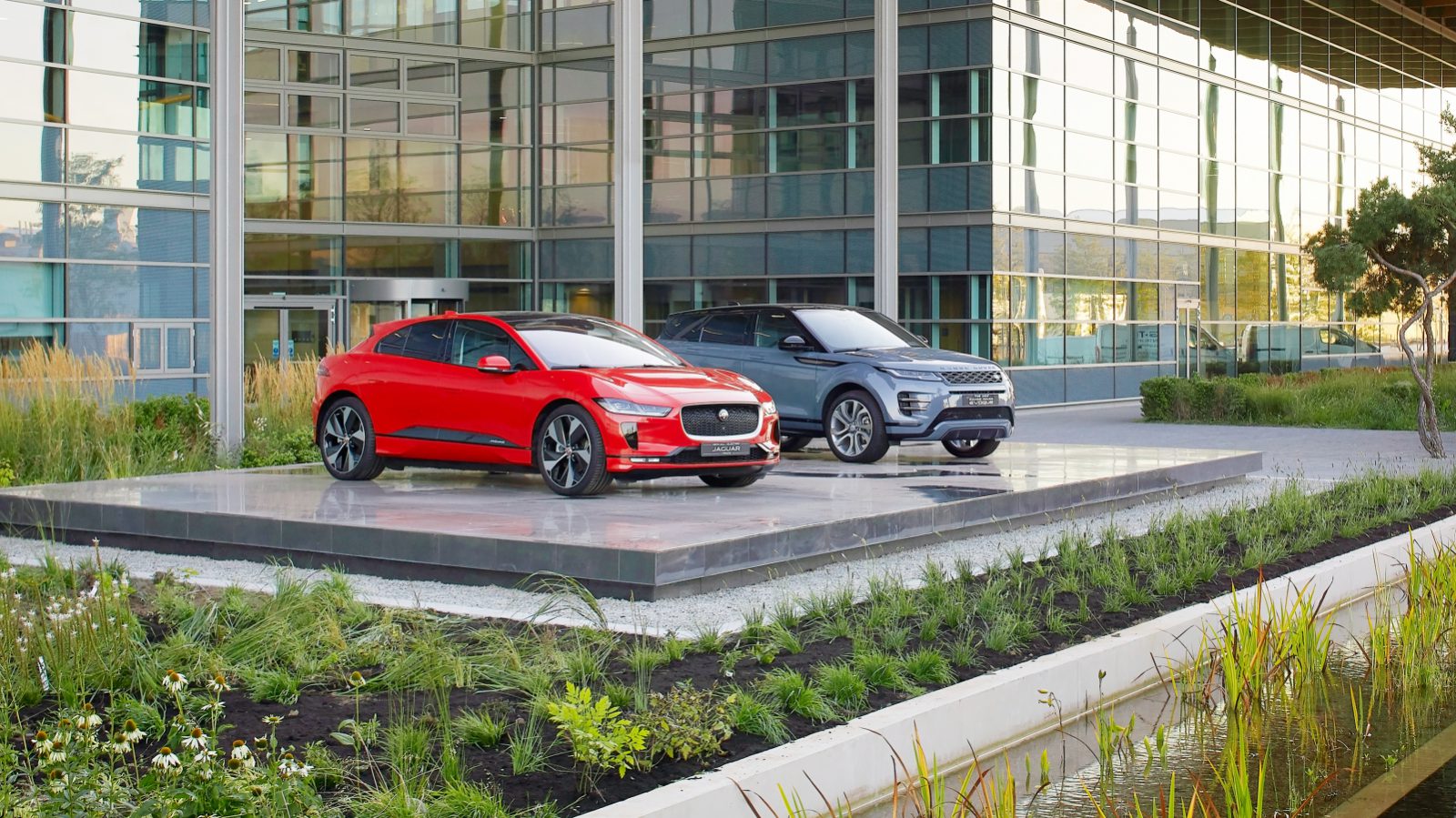 Twee rode Jaguar SUV's geparkeerd voor een gebouw.