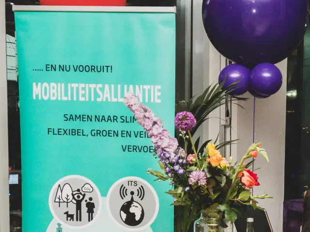 Een Mobiliteitsalliantie spandoek met ballonnen en bloemen voor een raam.
