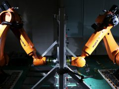 Twee oranje Nissan-robots werken samen in een fabriek.