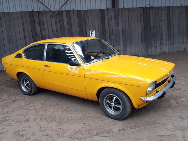 Een oude gele Opel staat geparkeerd in een garage.