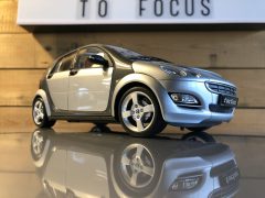 Een zilveren Smart Forfour-speelgoedauto staat op een tafel naast een bord met de tekst 'focus'.