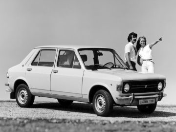 Een zwart-witfoto van een man en vrouw die naast een Fiat 128 staan.