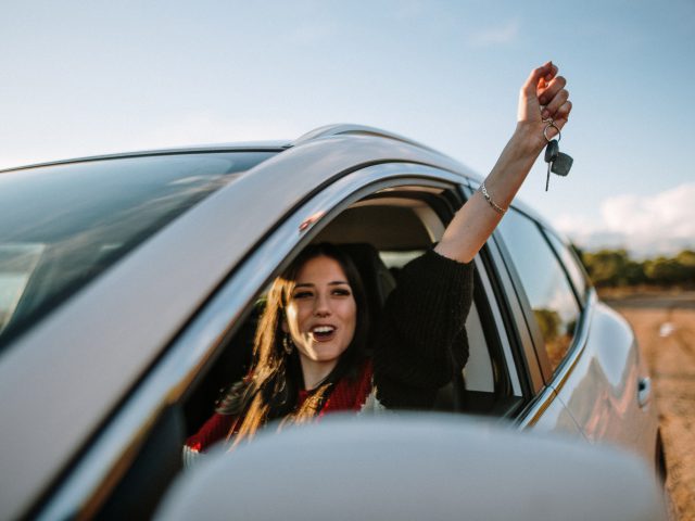 Een vrouw in een witte auto zwaait met haar handen in de lucht, klaar om uit te lenen.