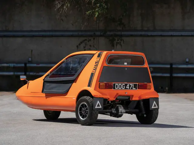 Een kleine oranje Bond Bug geparkeerd op een parkeerplaats.