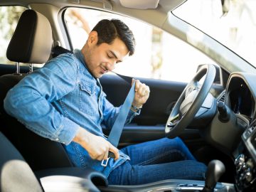 Een man zit in zijn auto met zijn veiligheidsgordel afgesteld, klaar voor een eersteklas vertrek.