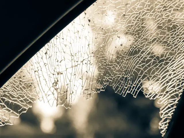 Een zwart-witfoto van een gebarsten ruit in een auto, als gevolg van vandalisme.