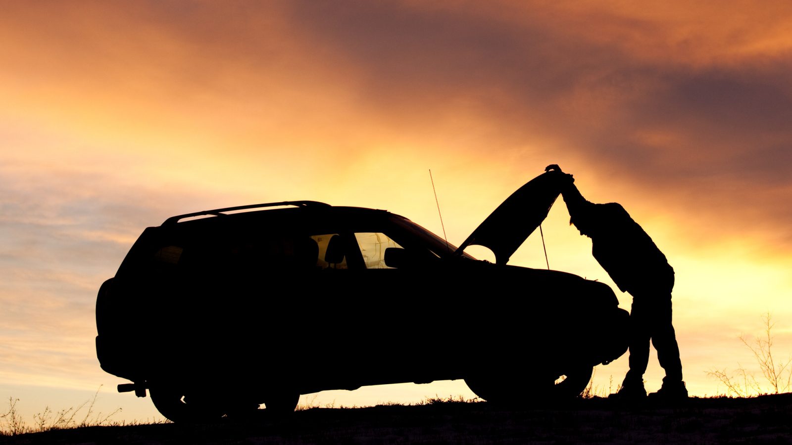 Silhouet van een man die de meest betrouwbare auto repareert bij zonsondergang.