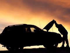 Silhouet van een man die de meest betrouwbare auto repareert bij zonsondergang.
