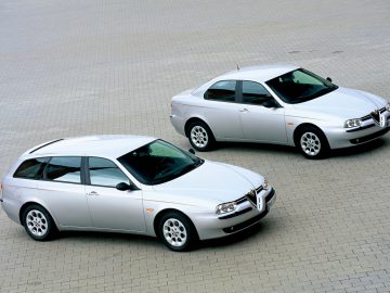 Twee zilveren Alfa Romeo 156 auto's geparkeerd op een parkeerplaats.