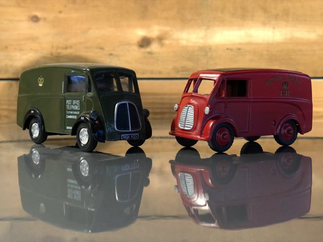 Twee Morris J Van speelgoedvrachtwagens op een houten oppervlak.