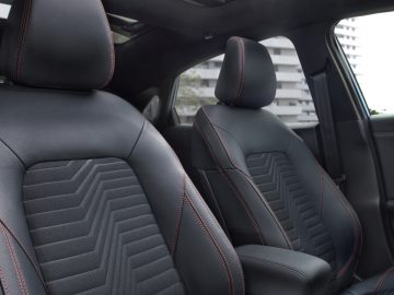Het interieur van een Ford Puma met zwart lederen stoelen en rode stiksels.