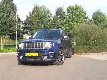 Een blauwe Jeep Renegade staat geparkeerd voor een boom.