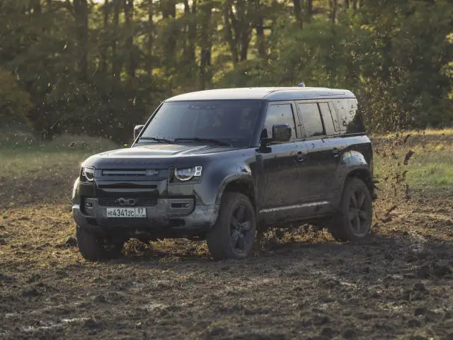 De James Bond-landroververdediger rijdt door een modderig veld.