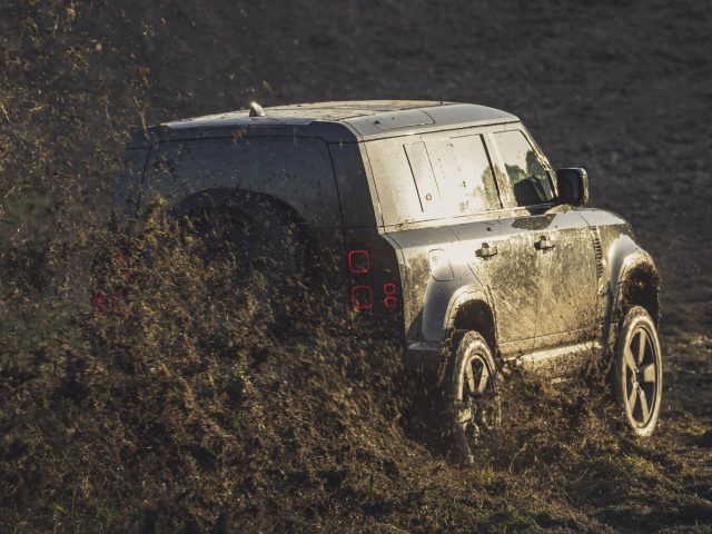 Een zwarte landroververdediger, die doet denken aan een James Bond-voertuig, rijdt door de modder.