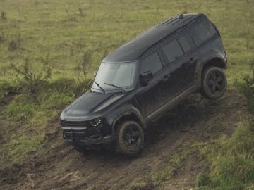 De James Bond Land Rover Defender rijdt een modderige heuvel af.