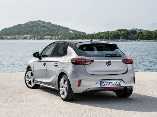 De achterkant van een zilverkleurige Opel Corsa geparkeerd vlakbij een watermassa.
