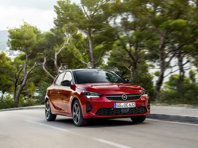 De rode Opel Corsa rijdt over een weg.