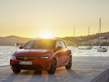 Een rode Opel Corsa geparkeerd op een kade bij zonsondergang.