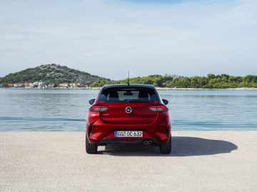 De achterkant van een rode Opel Corsa geparkeerd nabij een watermassa.