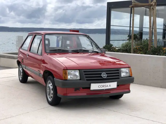 Een kleine rode Opel Corsa geparkeerd voor de oceaan.
