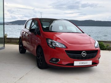 Een rode Opel Corsa geparkeerd voor de oceaan.