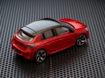 Een rode Opel Corsa speelgoedauto op een metalen oppervlak.
