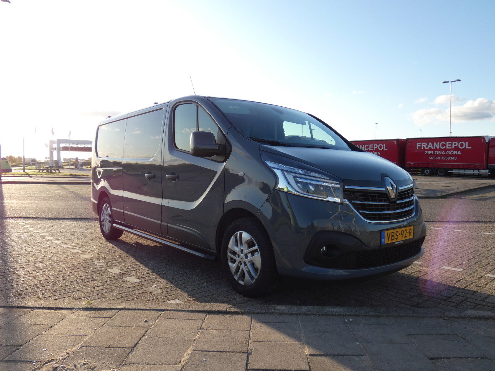 Langs de kant van de weg staat een grijs Renault-busje geparkeerd.