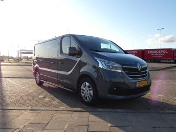 Langs de kant van de weg staat een grijs Renault-busje geparkeerd.