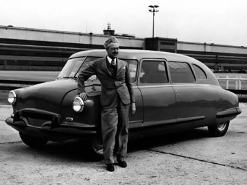 Een man in pak staat naast een oude Stout Scarab.