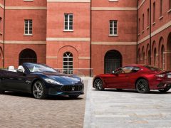 Twee Maserati GranTurismo-sportwagens geparkeerd voor een bakstenen gebouw.
