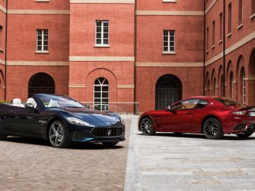 Twee Maserati GranTurismo-sportwagens geparkeerd voor een bakstenen gebouw.