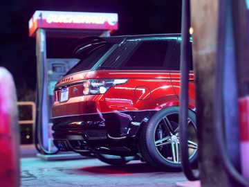 Een rode landrover uit Need for Speed Heat staat geparkeerd bij een benzinestation.