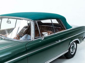 In een witte kamer staat een oude groene Mercedes-Benz geparkeerd.