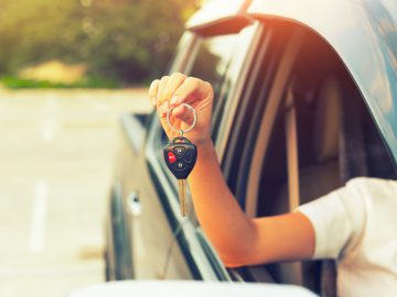 Een vrouw die een autosleutel uit het raam van een nieuwe auto houdt.