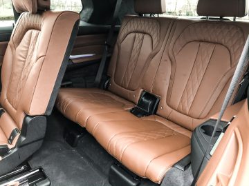 De achterbank van een BMW X7 met bruin lederen stoelen.