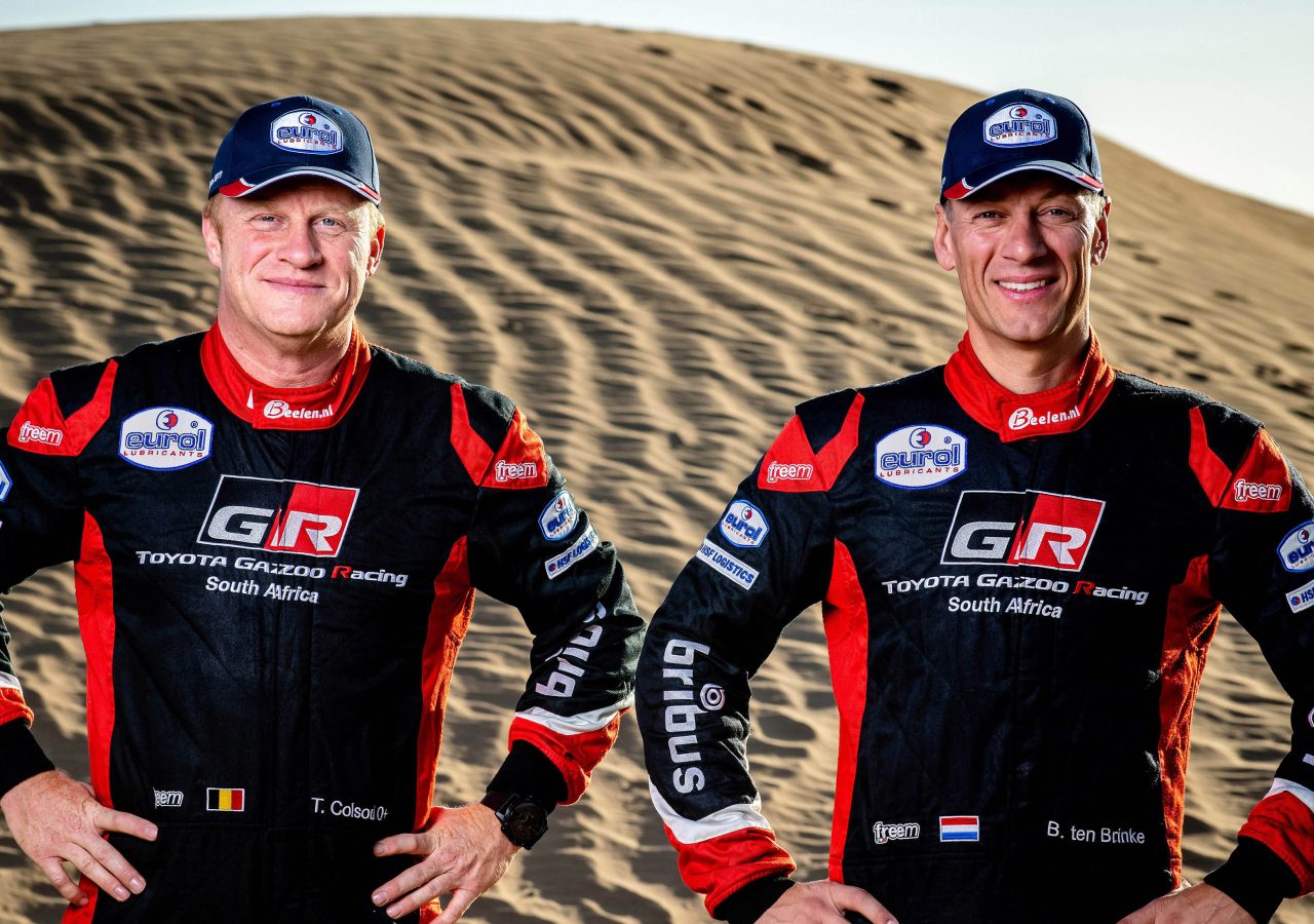 Bernhard ten Brinke en een andere man poseren voor een zandduin.