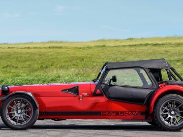 Een rode Caterham Seven 485 CSR-sportwagen staat geparkeerd aan de kant van een weg.