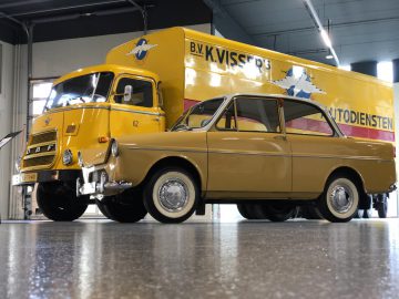 In de garage van het DAF Museum staat een gele auto naast een vrachtwagen geparkeerd.