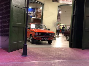 Voor een groene deur bij het DAF Museum staat een oranje auto geparkeerd.